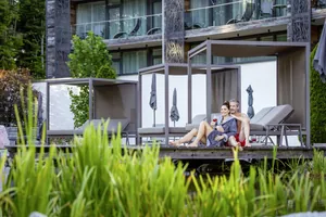 Paar entspannt sich auf einer Holzterrasse im Außenbereich des Wellness & Naturresort Reischlhof mit gemütlichen Daybeds im Hintergrund