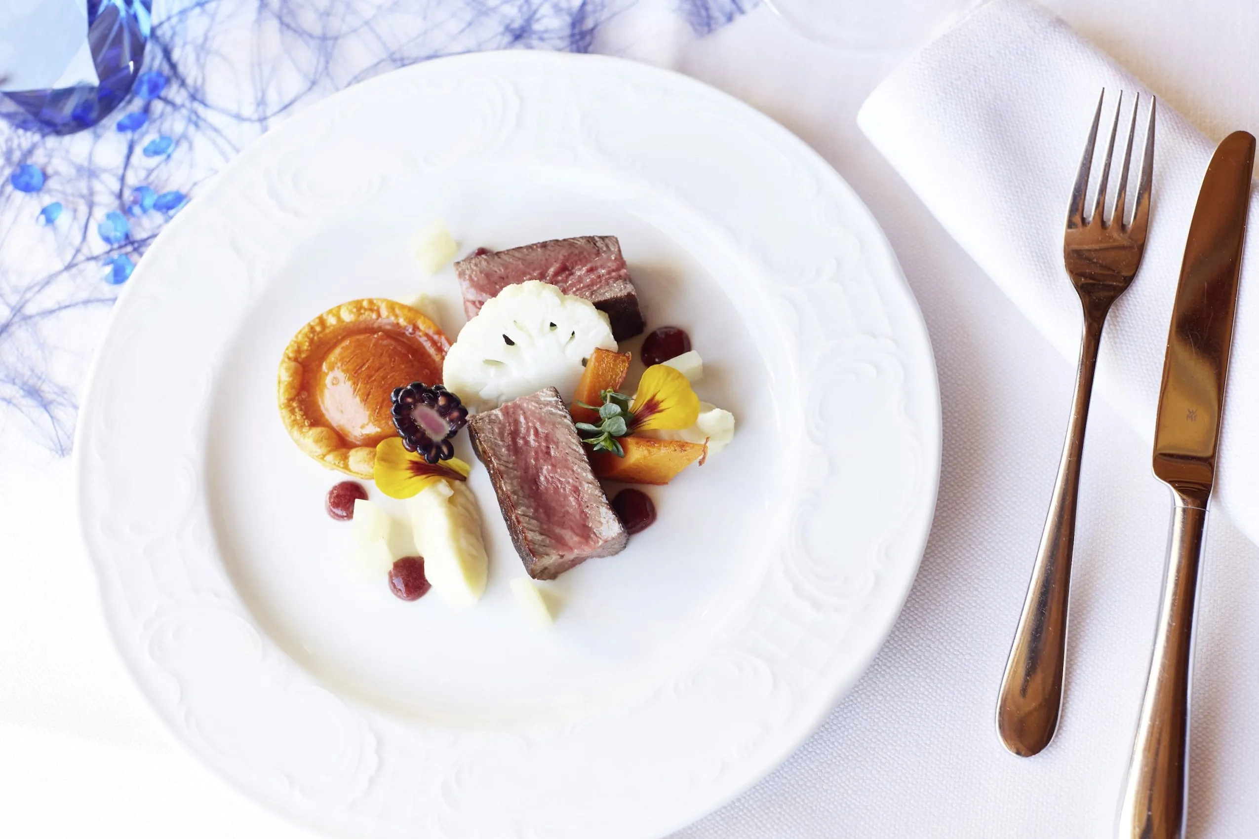 Wei&szlig;es Teller auf wei&szlig;er Tischdecke mit sch&ouml;n angerichtetem Gourmetessen.