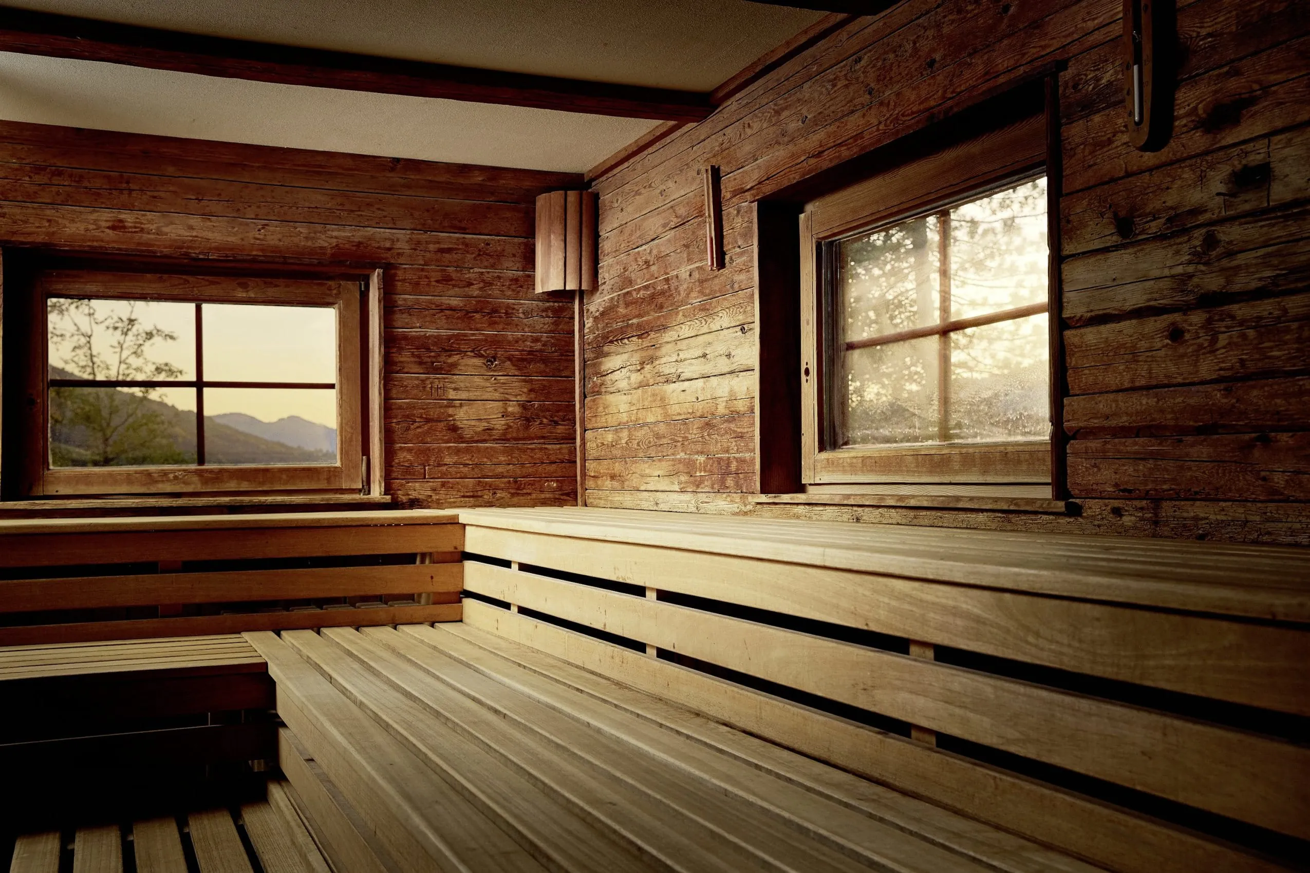 Sauna mit uriger Holzverkleidung und kleinen Fenstern nach drau&szlig;en, wo die Berge und B&auml;ume zu sehen sind.
