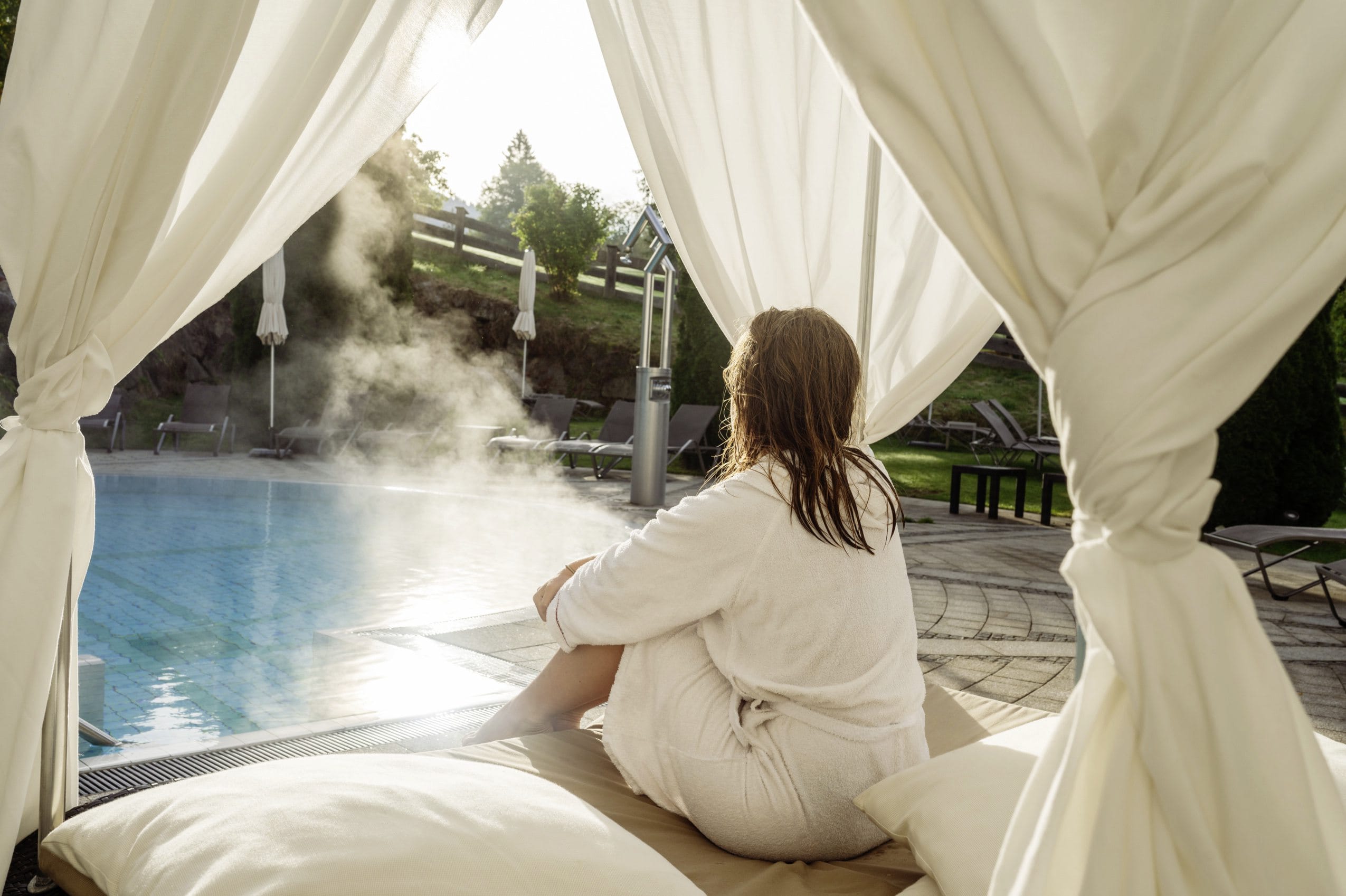 Eine Frau entspannt nach dem Schwimmen im Bademantel auf den Daybeds des Tiroler Wellnesshotels A-Rosa in Kitzbühel.