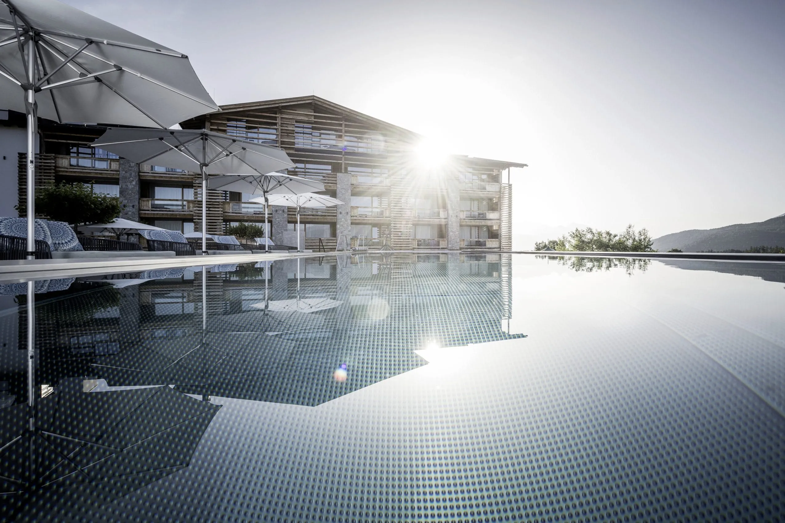 Die Sonne blitzt &uuml;ber das Dach des Alpenresort Schwarz und spiegelt sich im Infinity-Pool des Tiroler Wellnesshotels wieder.