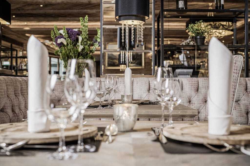 Edel gedeckter Tisch mit Weingläsern, Silberbesteck und großen weißen Stoffservietten im modern eingerichteten Restaurant des Alpin Resort Sacher.