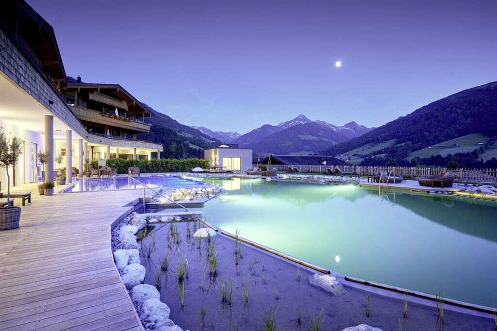Der Außenpool mit angrenzender Terrasse des Wellnesshotels der Böglerhof in Tirol bei Dämmerung.