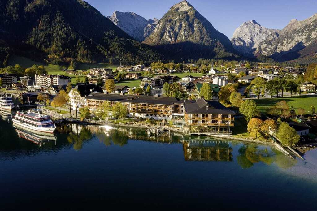 Luftaufnahme des Fürstenhaus Achensees. Direkt vor dem Hotel ankern Schiffe auf dem Achensee während sich hinter dem Hotel eine wunderschöne Berglandschaft erstreckt.