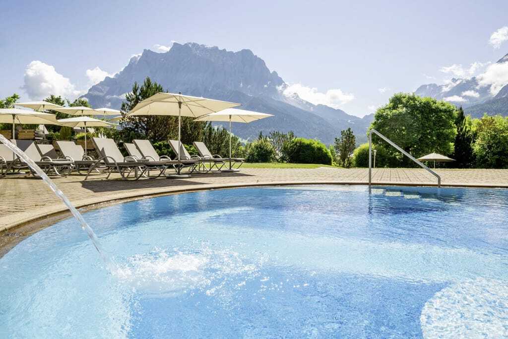 Strahlend türkisblauer Pool mit Blick auf die Tiroler Gebirge vom Wellnesshotel Post Lermoos aus.