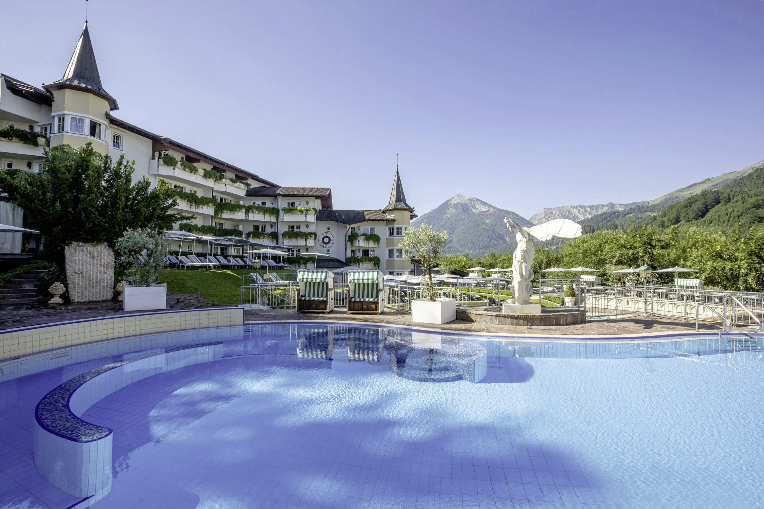 Außenansicht des Posthotels Achenkirch mit dem großen Outdoorpool im Vordergrund und Bergen und Wälder im Hintergrund.