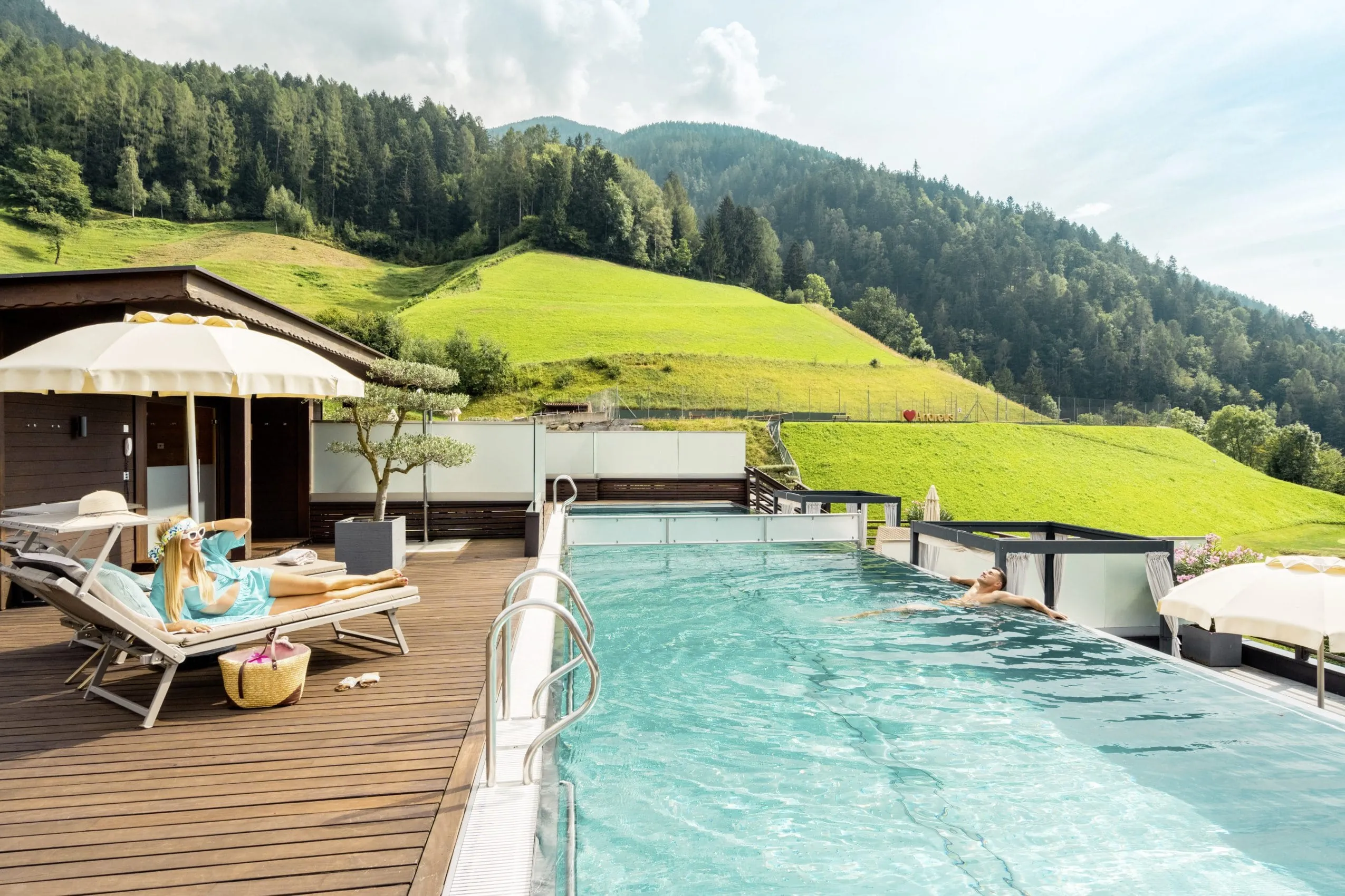 Outdoorpool mit angrenzender Holzterrasse umringt von saftigen gr&uuml;nen Wiesen und B&auml;umen.