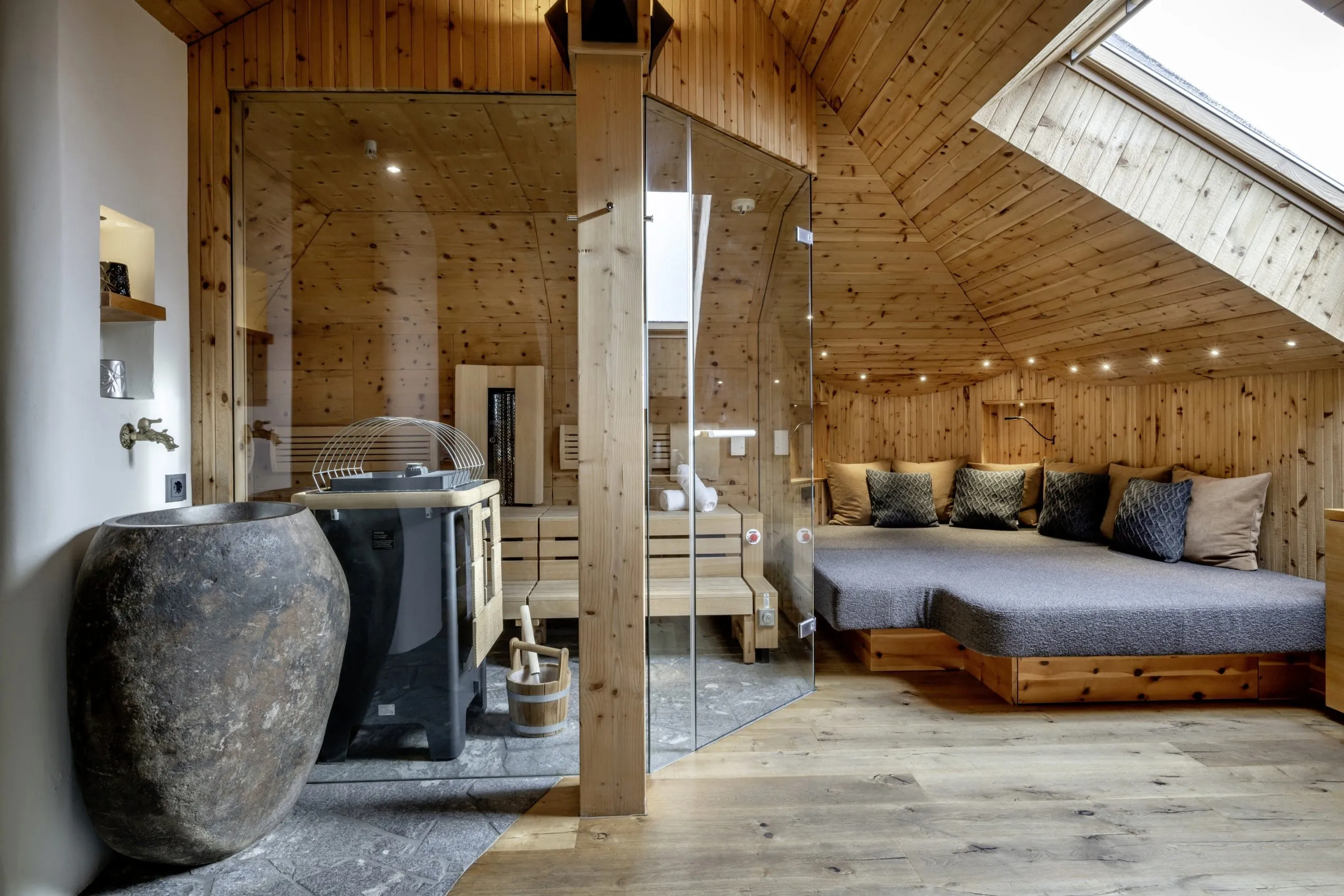 Sauna zwei W&auml;nden komplett aus Glas. Davor liegt eine gro&szlig;e Ruhe-Lounge mit zahlreichen gem&uuml;tlichen Kissen und Leselampe.