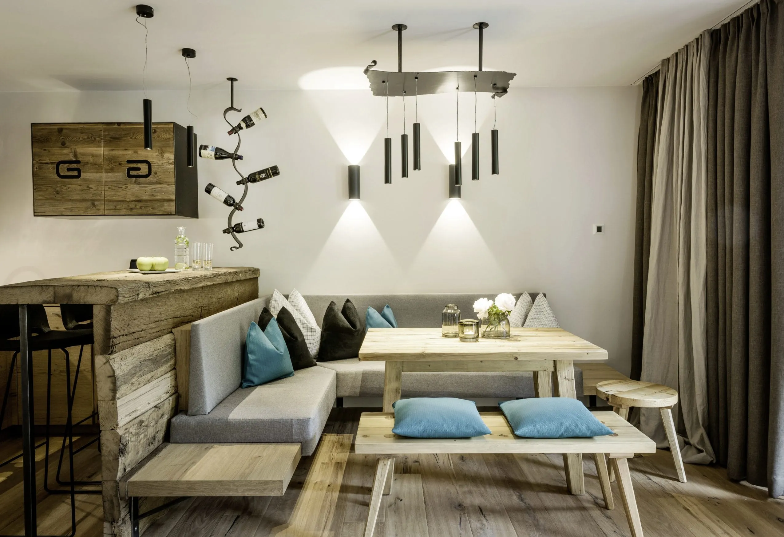 Wohnbereich mit Holztheke und schwarzen hohen Barhockern. Davor liegt eine gem&uuml;tliche Sitzecke mit Eckbank und Esstisch.