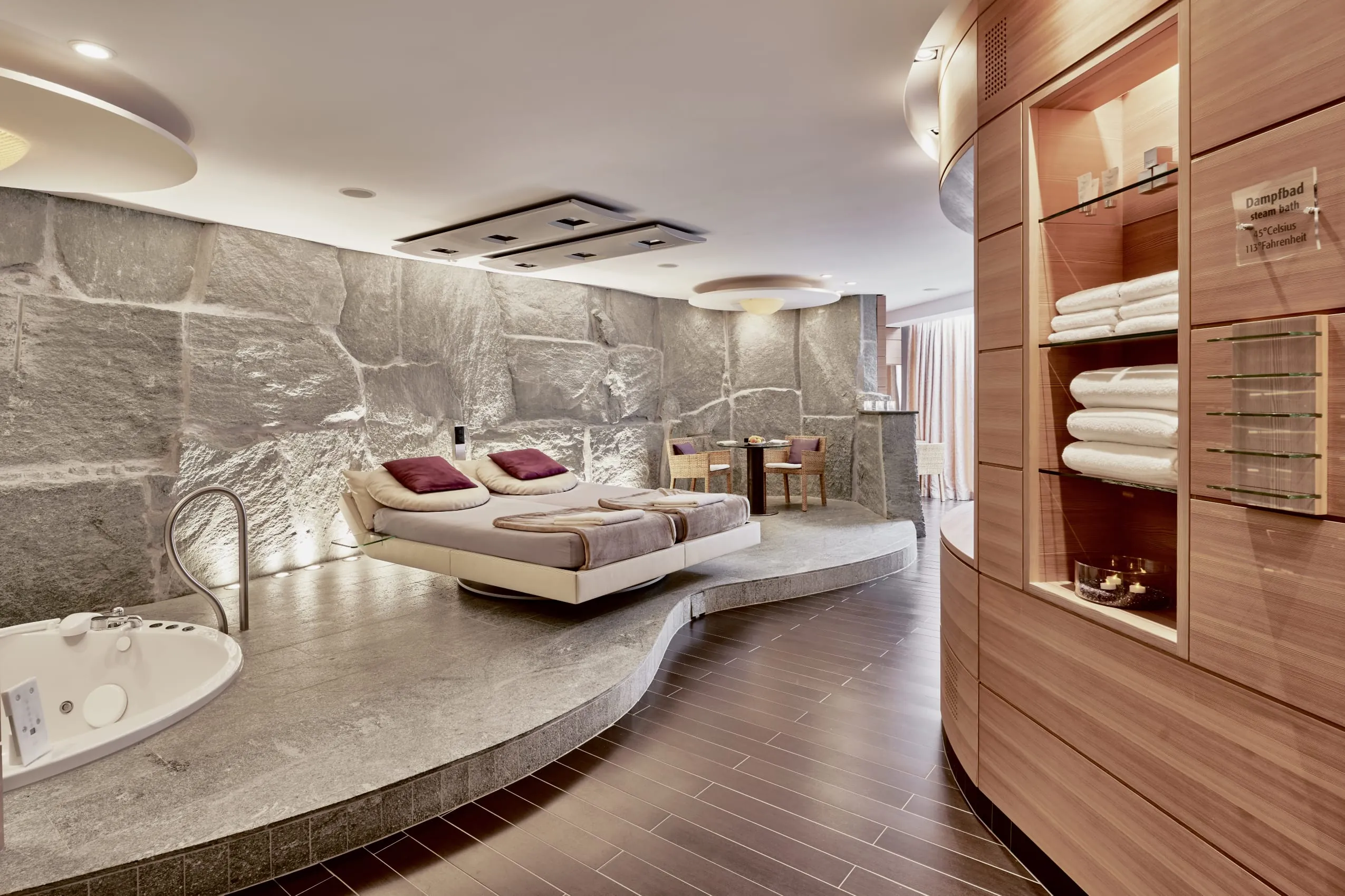 Private Spa im Grand Hotel Bad Ragaz mit gro&szlig;en grauen Natursteinen an der Wand, mit in den Boden eingelassenen Whirlpool, danebenliegender Ruheliege.