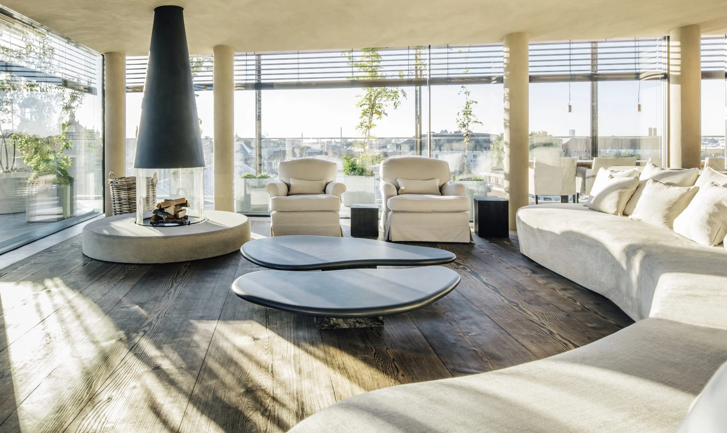 Bodentiefe Panorama-Fenster rund um den Wohnbereich mit Blick &uuml;ber M&uuml;nchen. Design-Kamin und gro&szlig;e gem&uuml;tliche wei&szlig;e Polsterm&ouml;bel.