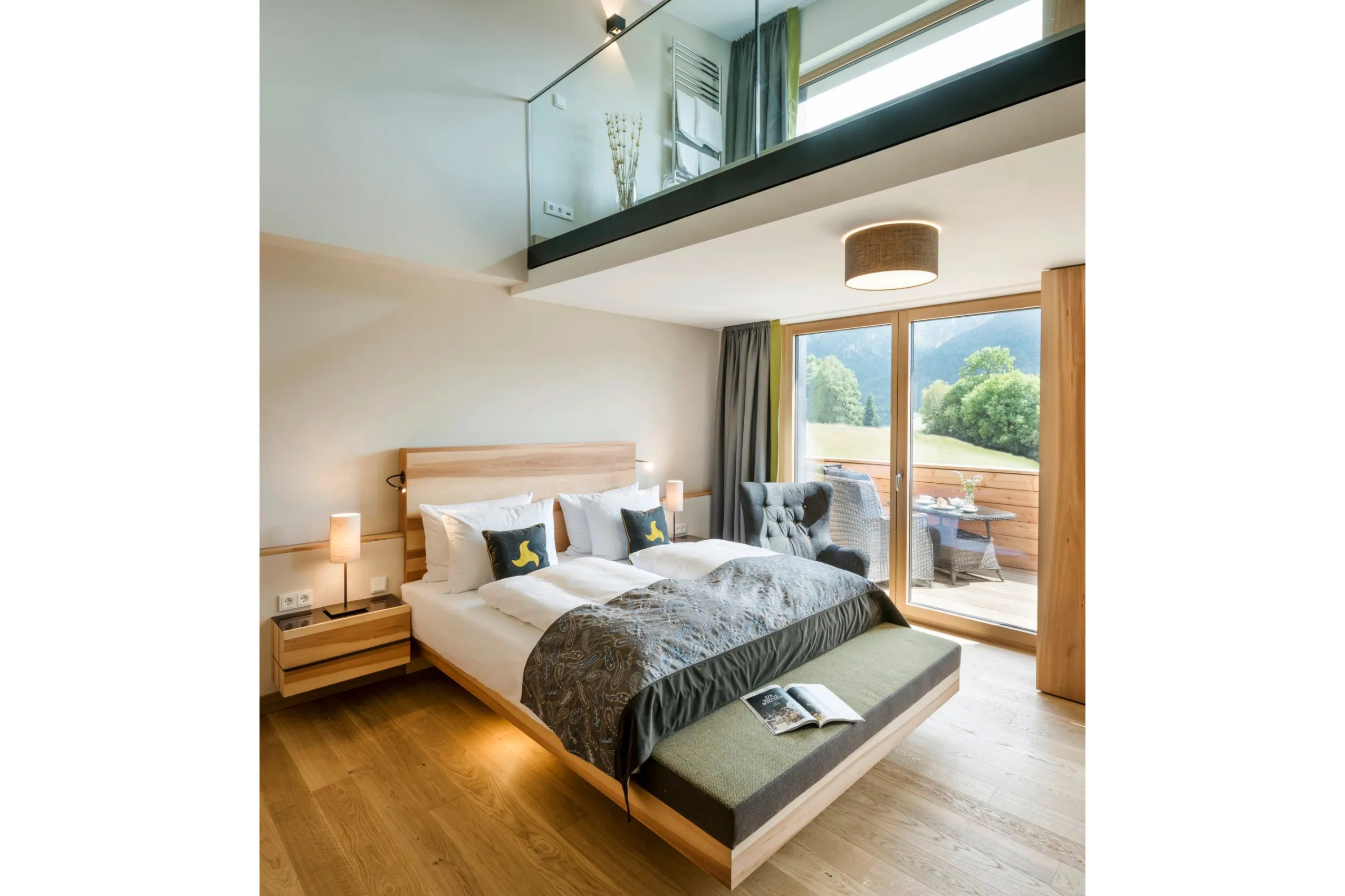 Helles Schlafzimmer mit Doppelbett und gro&szlig;er Balkont&uuml;r mit dar&uuml;ber liegender Wellnessgalerie.