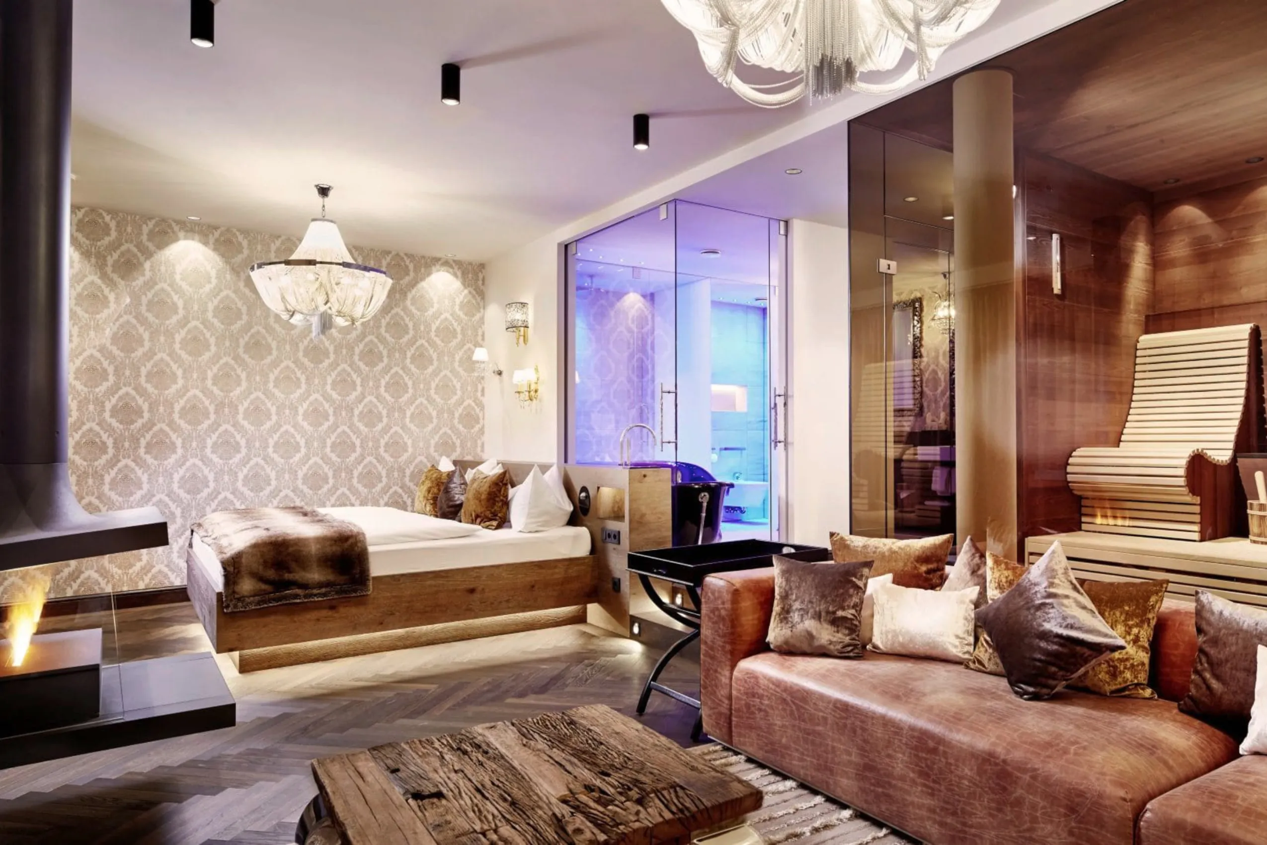 Privat Wellness Suite mit gro&szlig;z&uuml;gigem Badezimmer und Sauna abgetrennt durch eine Glaswand vom Wohnbereich mit Schlafzimmer, gro&szlig;em Sofa und Kamin.