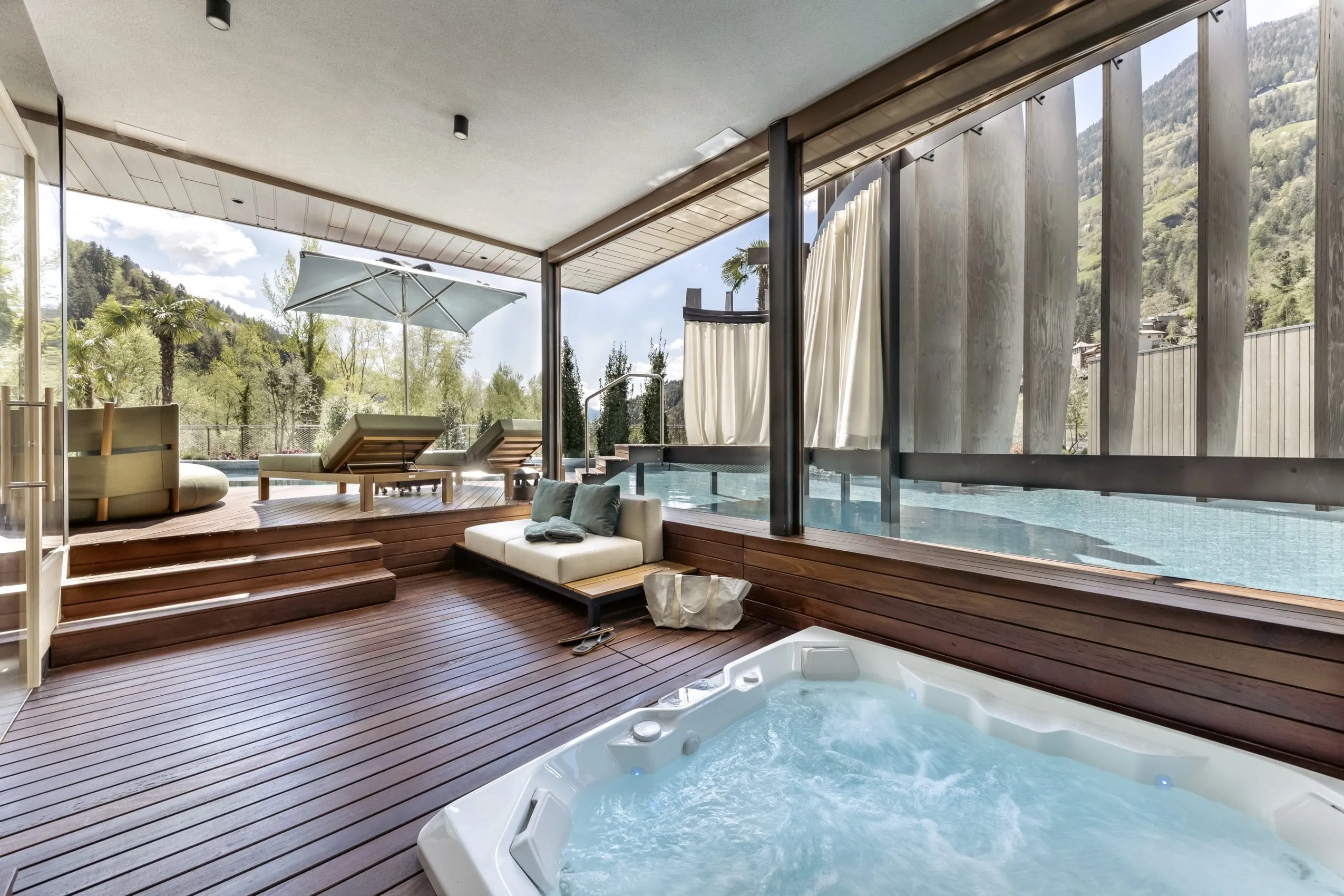 &Uuml;berdachter in den Boden eingelassener Whirlpool. Au&szlig;en liegt die Terrasse mit Ruheliegen und angrenzendem Pool.