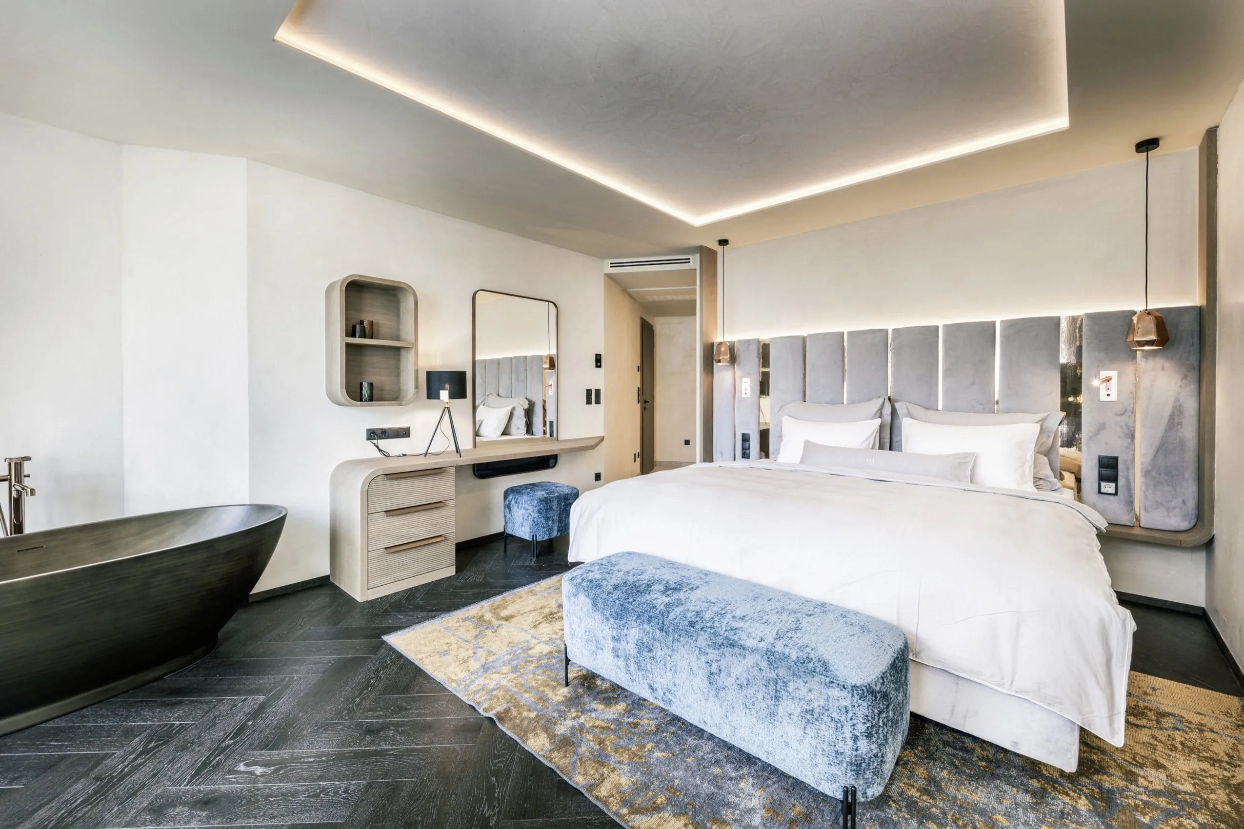 Schlafzimmer der See Villa Deluxe mit Kingsizebett, schicken Polsterm&ouml;beln und freistehender Badewanne neben dem Bett in dunkler Holzoptik.