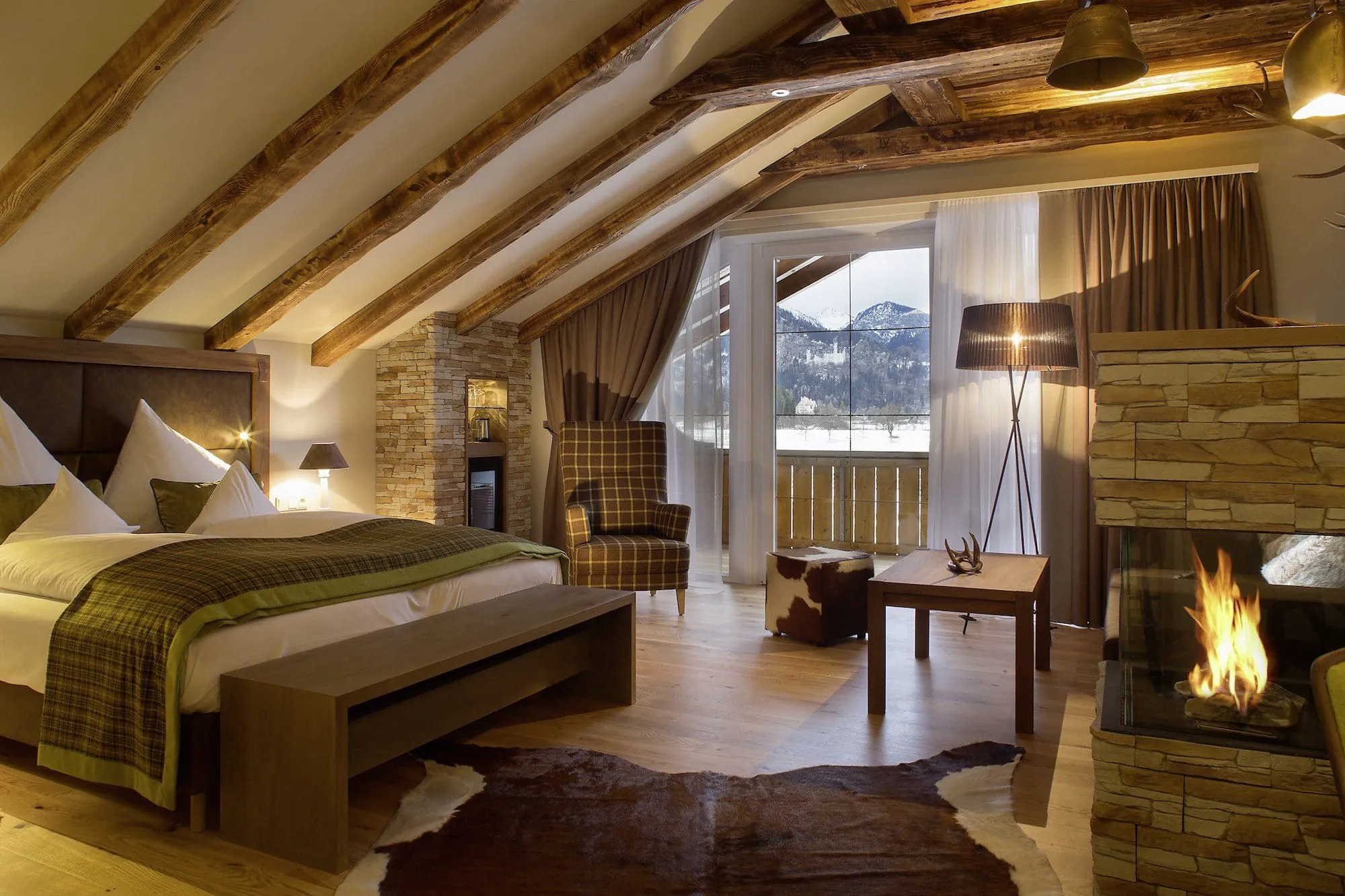 Urig eingerichtete Suite mit massiven Holzbalken an der Decke, Kamin, Kuhfellteppich und Hirschgeweih an der Wand