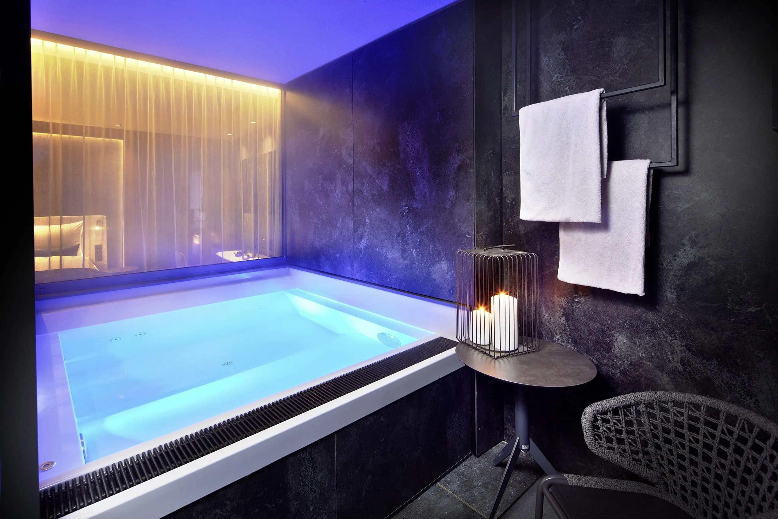 Edle schwarze Marmorfliesenwand und Boden mit quadratischem Whirlpool mit stimmungsvoller Beleuchtung.