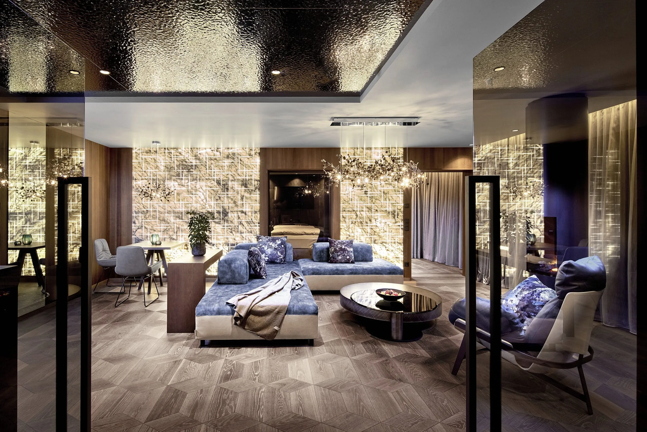Wohnbereich der Typ A Luxury Private Wellness Suite. Luxuri&ouml;se Einrichtung mit blauen Polsterm&ouml;beln und indirekt beleuchtenden goldenen W&auml;nden.