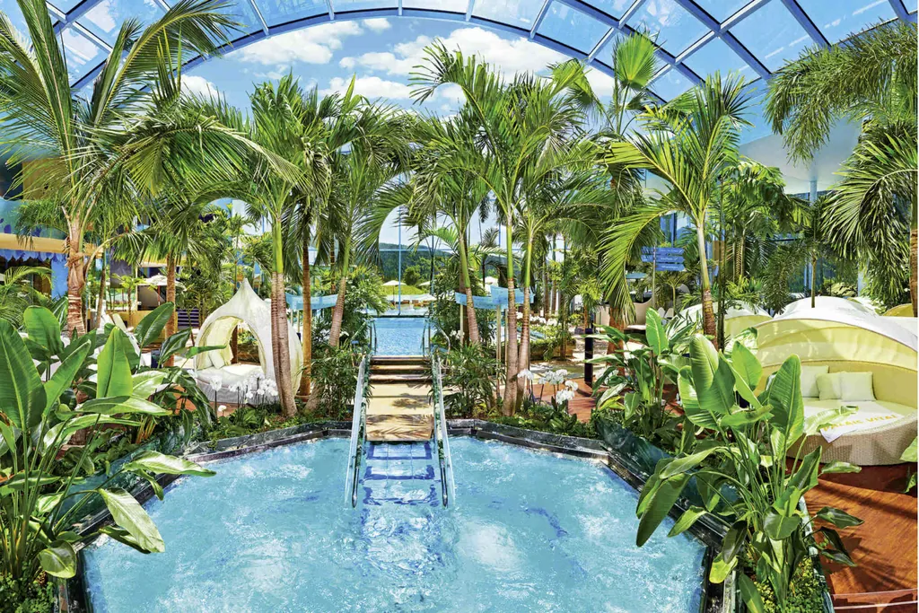 Einzelne Becken mit hellblau schimmerndem Wasser umringt von Palmen und gemütlichen Daybeds im Badeparadies Schwarzwald