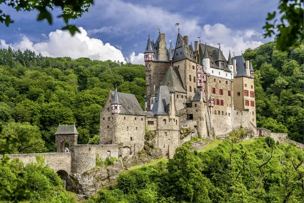 Historische Burg wie aus dem Bilderbuch mit zahlreichen Türmchen. Sie thront auf einem Hügel umgeben von Bäumen und Sträuchern.