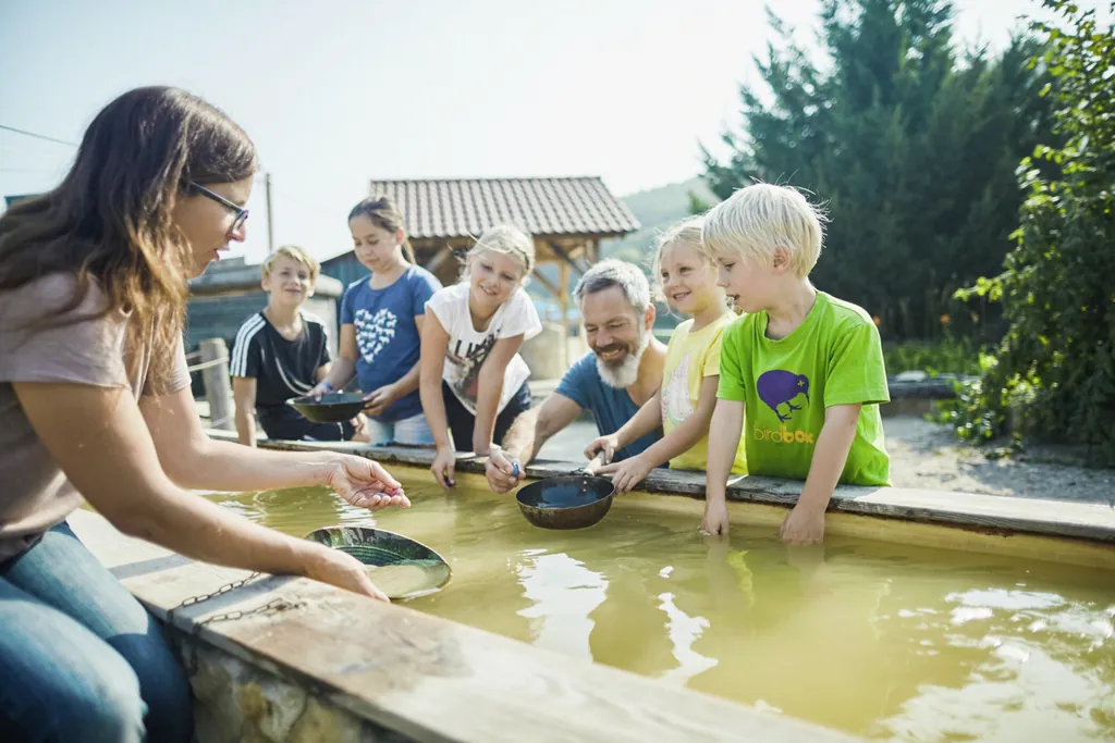 Kinder stehen fröhlich an einem Schürfbecken mit Schürftellern und suchen nach Gold und anderen Edelsteinen im Edelsteinpark Pielachtal.