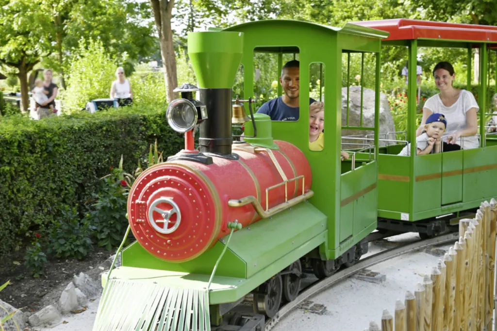 Junge Familie mit zwei kleinen Kindern die in einem Fahrgeschäft mit einer kleinen grünen Lokomotive fahren.