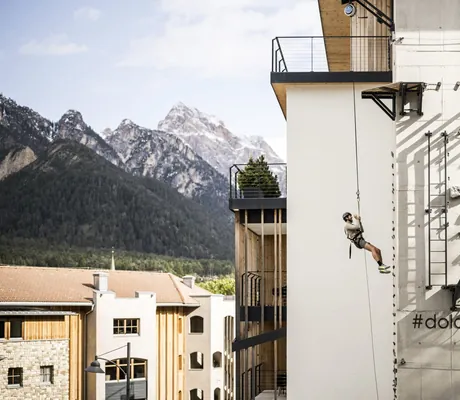 Mann hängt am Seil der Kletterwand des Excelsior Dolomites Life Resort