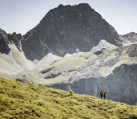zwei Personen stehen auf Wiese vor monumentalem Felsmassiv im Tiroler Oberland