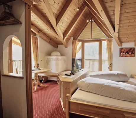 Giebelzimmer im Hotel Traube mit Holzwand hinter dem Bett und weißem Kamin