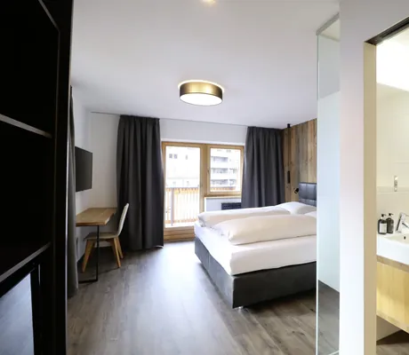 Zimmer im Hotel Traube mit runder goldener Deckenleuchte und Blick ins Badezimmer