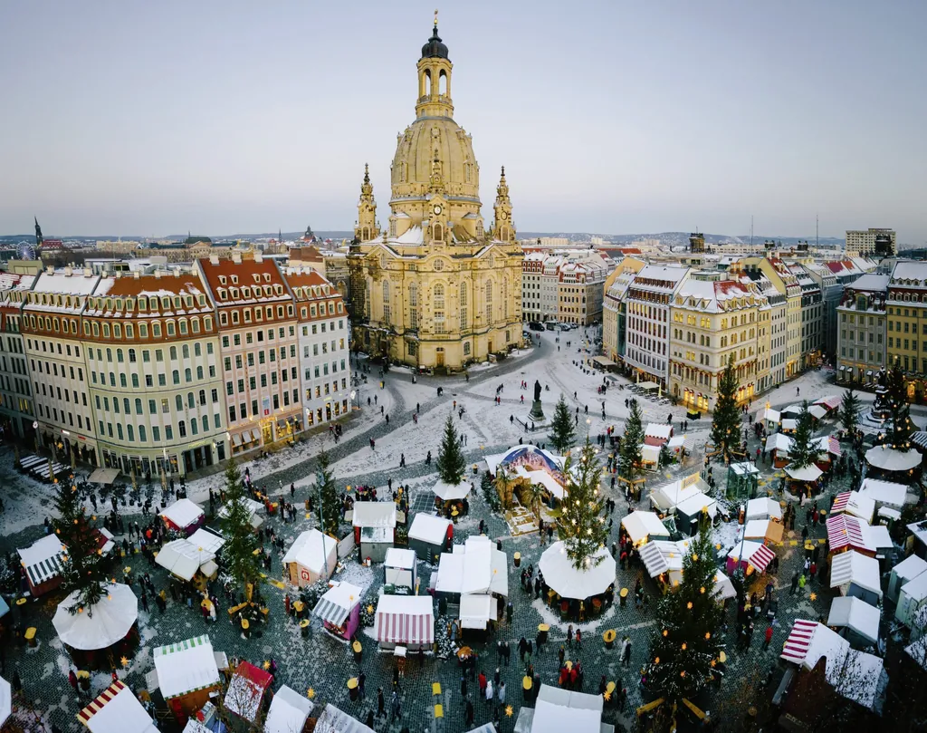 Blick auf den leicht eingeschneiten Neumarkt in Dresden mit festlich geschm&uuml;ckten H&uuml;tten und beleuchteten Weihnachtsb&auml;umen und Frauenkirche im Hintergrund