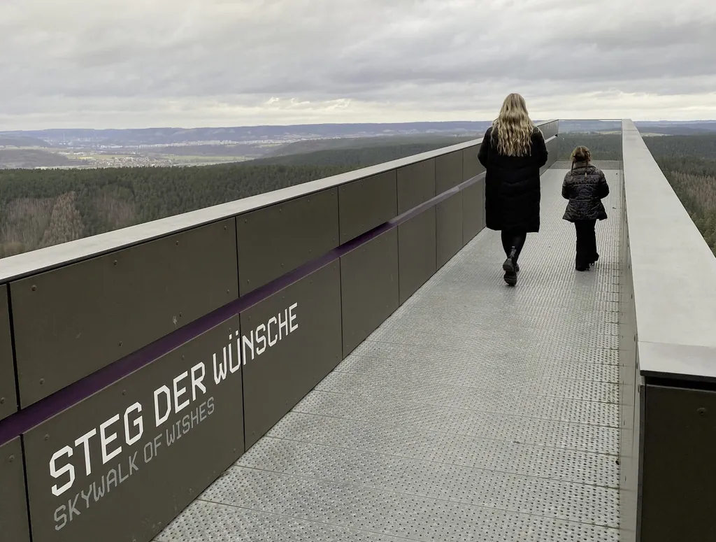 blonde Frau und kleines M&auml;dchen laufen auf dem langen Steg der W&uuml;nsche mit weitem Blick auf die umliegende Landschaft