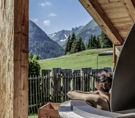 braunhaarige Frau lehnt sich aus dem Hot-Pot des Benglerwald Berg Chaletdorfs und schaut in die Berglandschaft