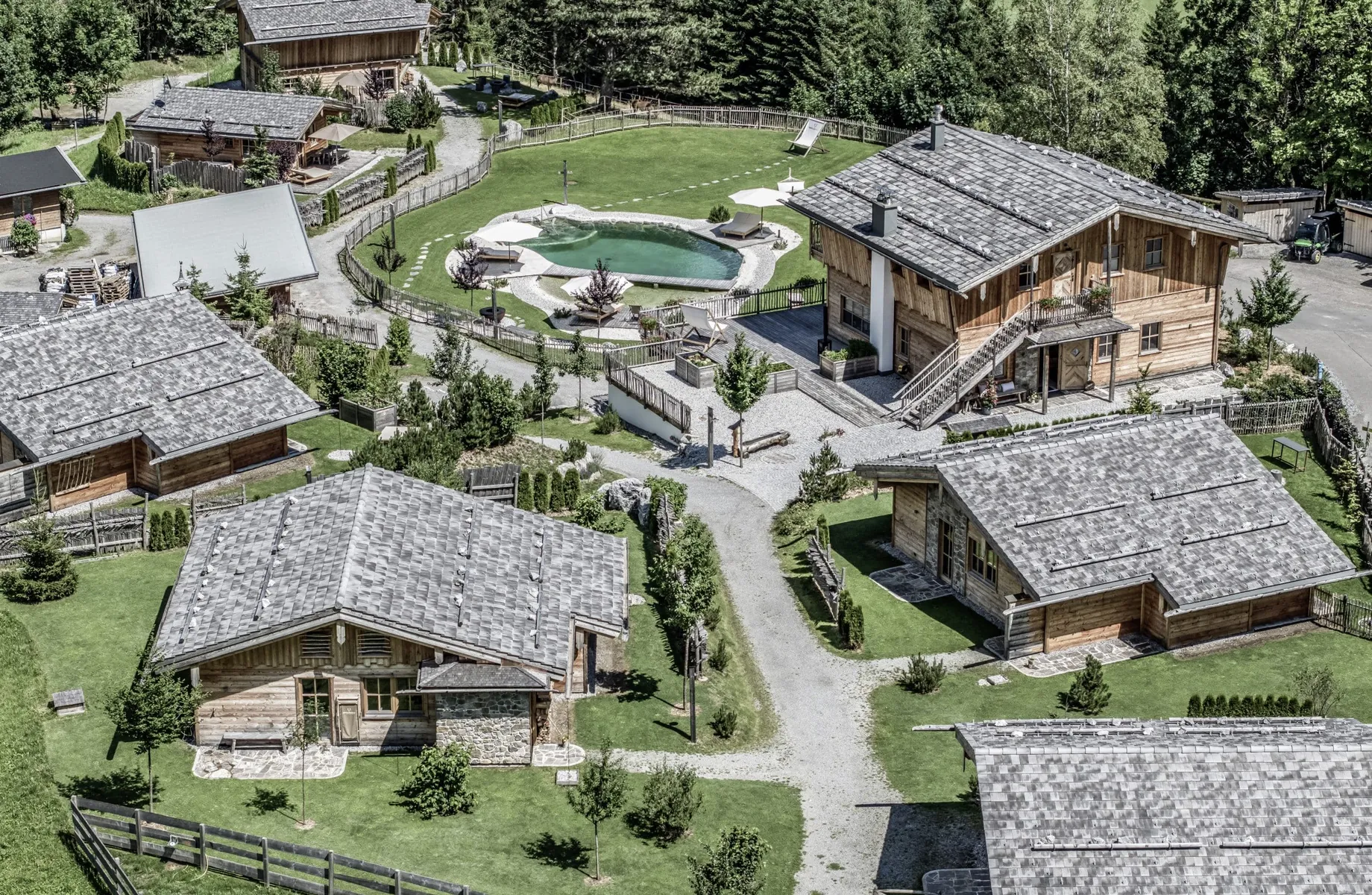 Aufnahme aus der Vogelperspektive des Benglerwald – Berg Chaletdorfs mit mehreren Hütten und Naturbadeteich
