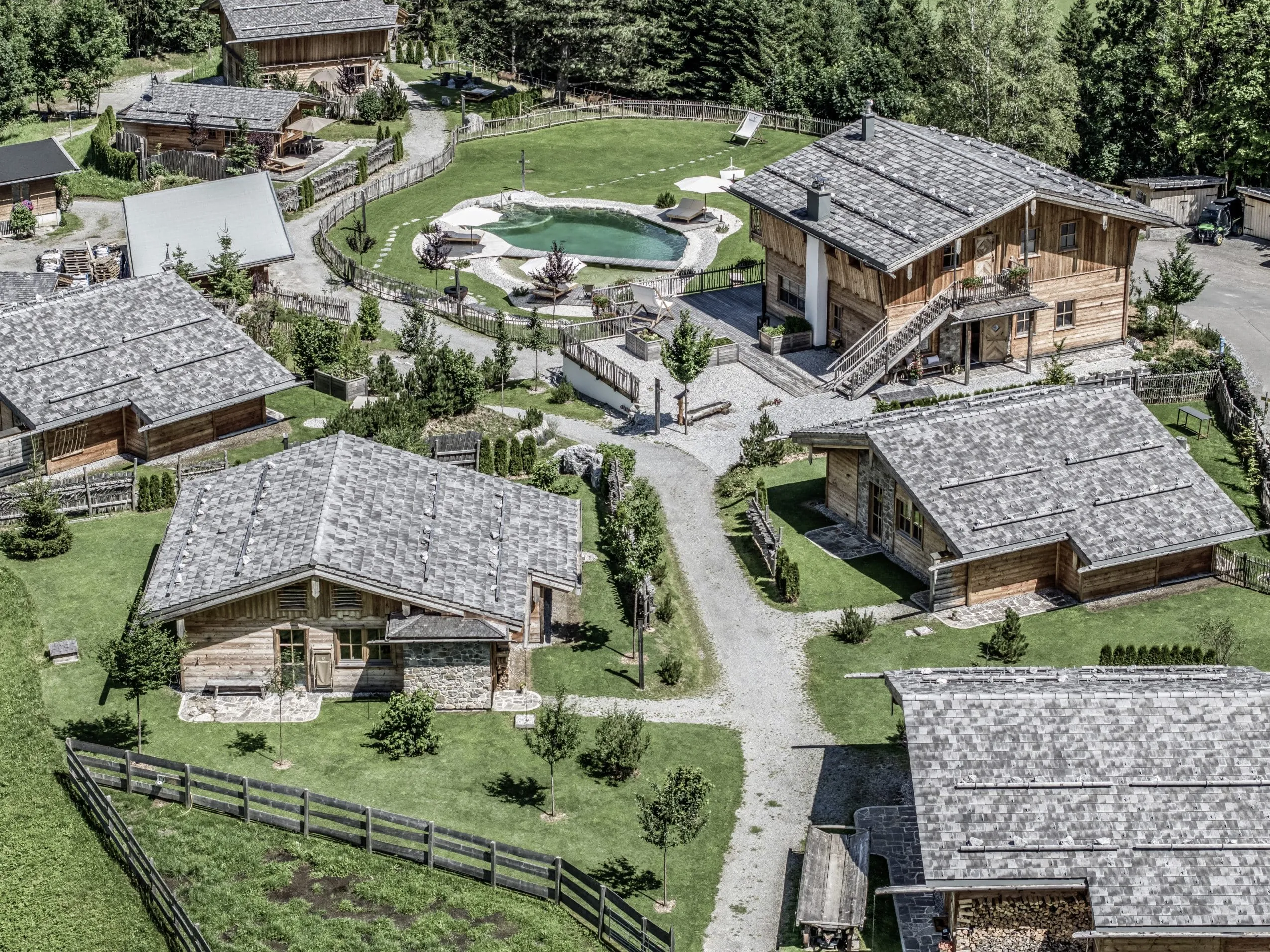 Aufnahme aus der Vogelperspektive des Benglerwald – Berg Chaletdorfs mit mehreren Hütten und Naturbadeteich