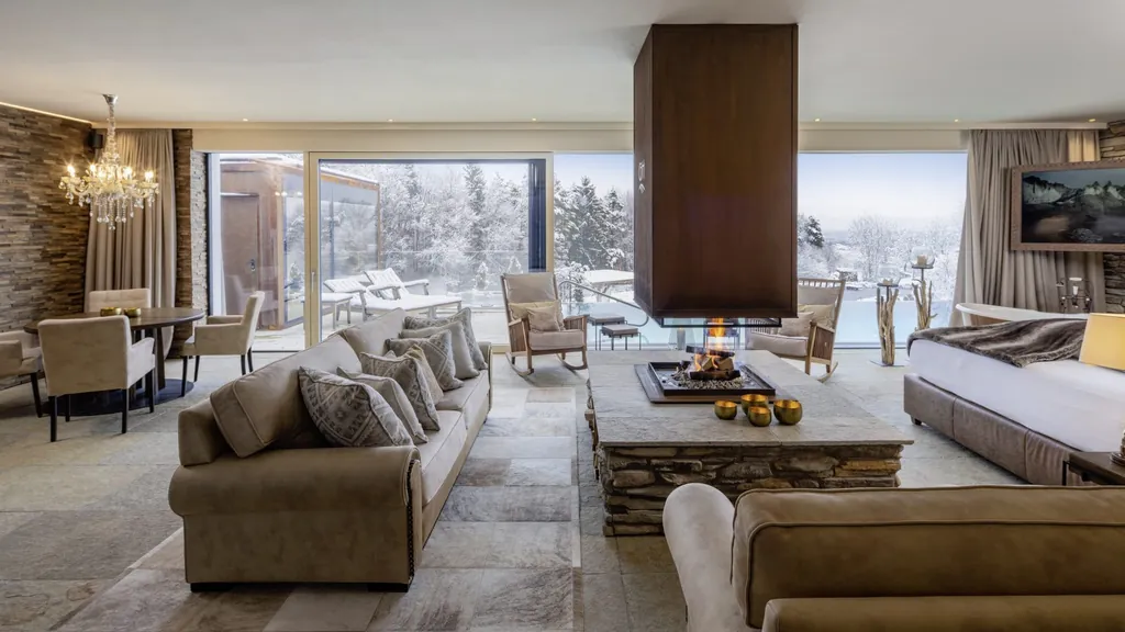 riesiger Wohnbereich mit offenem Steinkamin in der Mitte und langen beigen Sofas in den Golden Hill Chalets