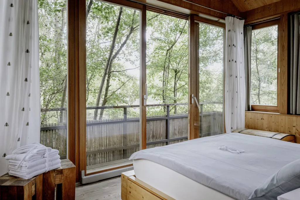 Doppelbett im Baumhaus des Hofgut Hafnerleiten mit großen Panoramafenstern und Waldblick