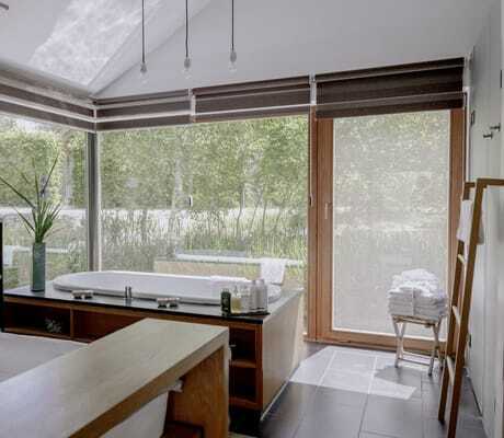 heller Raum mit Doppelbett, Holz-Schiebetisch und Badewanne direkt vor Panoramafenstern mit Blick in die grüne Natur auf dem Hofgut Hafnerleiten