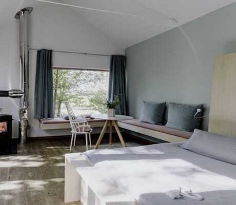 Doppelbett, gemütliche Sitzecke mit mintfarbener Wand, Kissen und Vorhängen, weißem Stuhl und kleinem Kamin auf dem Hofgut Hafnerleiten