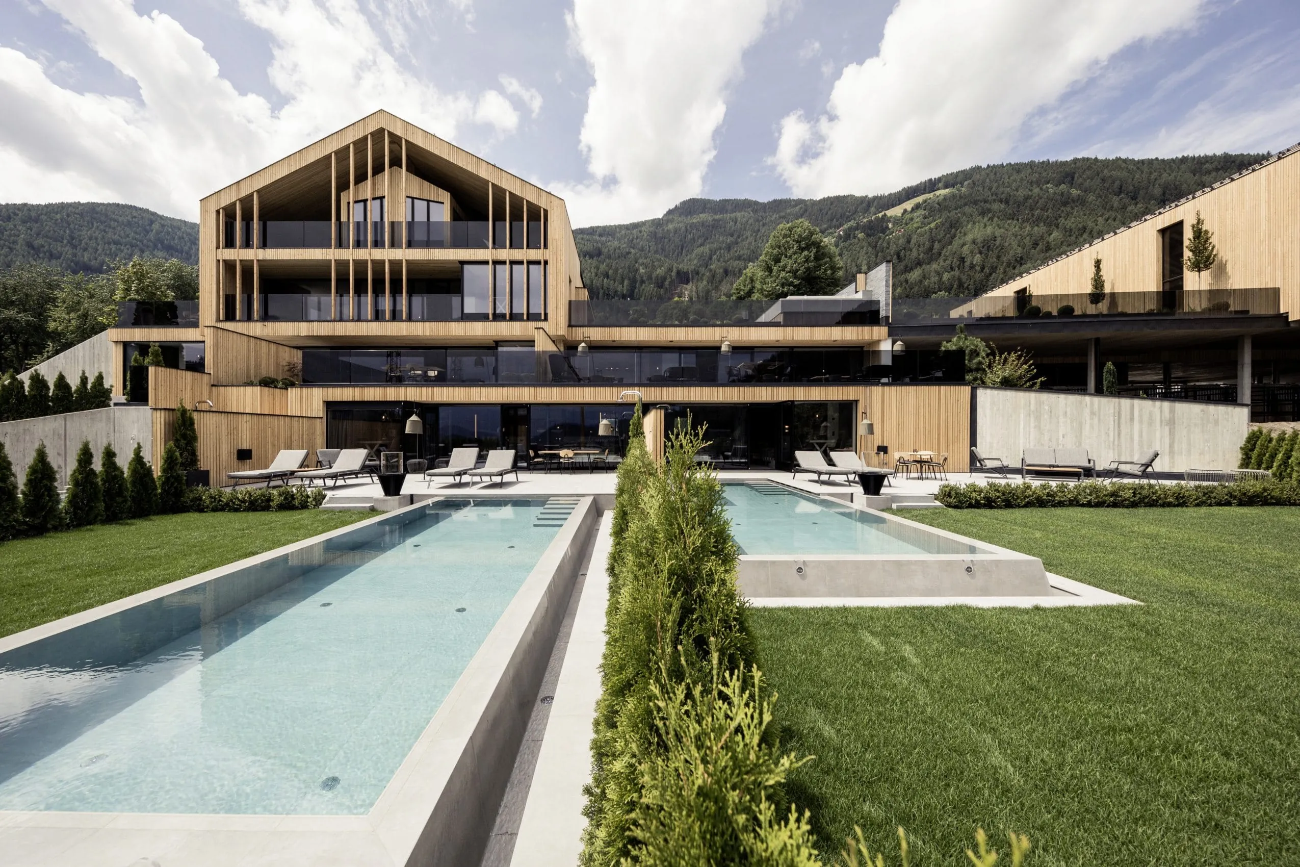 Holzfassade des PURMONTES Private Luxury Chalet mit Outdoorpools und Liegen