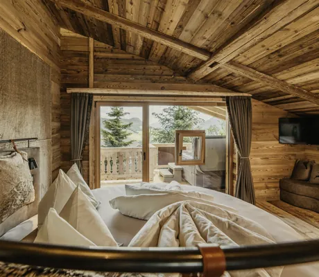Gemütlicher Wohnbereich in Altholz mit rundem Bett, Balkonblick auf die Berge, gemütlicher Sitzecke und TV