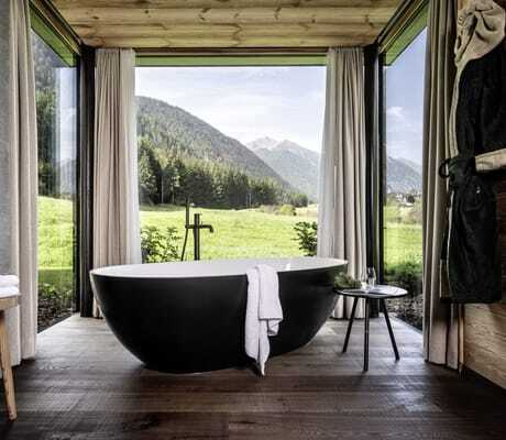 freistehende schwarze Badewanne in den Chalets Valsegg am Fenster zu grünen Wiesen und Wäldern