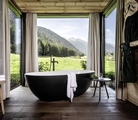 freistehende schwarze Badewanne in den Chalets Valsegg am Fenster zu grünen Wiesen und Wäldern