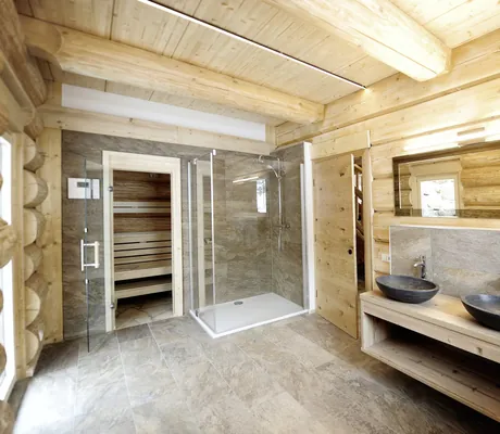 Badezimmer der Summit Lodges mit Holzwänden, zwei dunkelgrauen Stein-Waschbecken, Steinfließen-Boden, Regendusche und Sauna