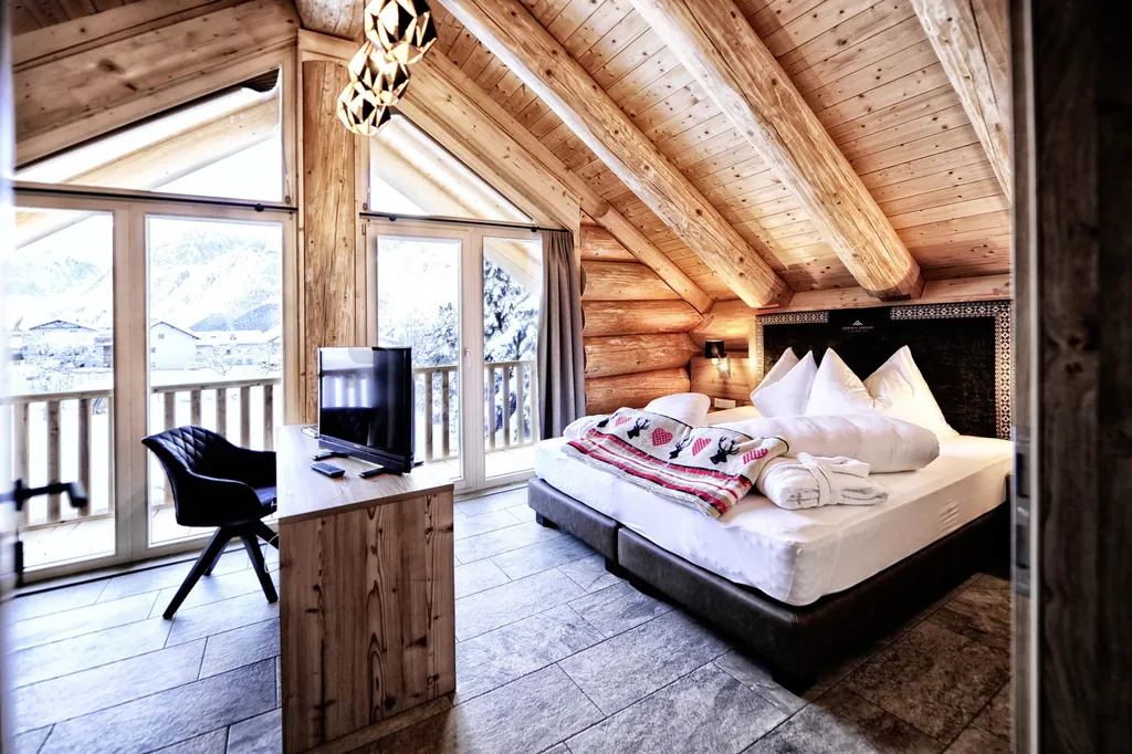 Schlafzimmer der Summit Lodges mit Holzwänden, Doppelbett, kleinem Fernseher und großen Fenstern mit Blick auf den Ort und die Berge