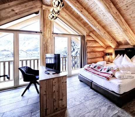 Schlafzimmer der Summit Lodges mit Holzwänden, Doppelbett, kleinem Fernseher und großen Fenstern mit Blick auf den Ort und die Berge