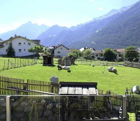 Blick auf die kleine Schaf-Weide vor den Summit Lodges sowie mehrere Häuser, Kirchturm und Berge im Hintergrund
