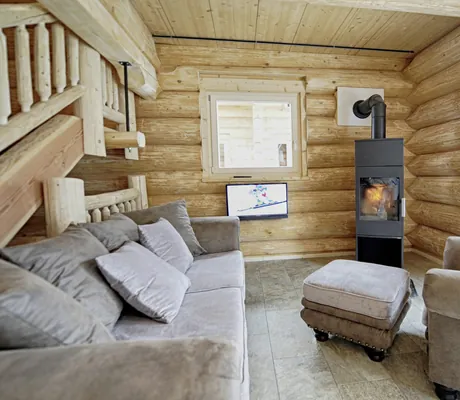 Gemütliches Wohnzimmer der Summit Lodges mit Holzvertäfelung, Kamin, grauem Sofa und Sessel und kleinem Fernseher an der Wand