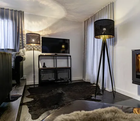 Wohnzimmer des Chalet vue au lac mit kleinem Kamin, zwei schwarzen Stehlampen, Fell auf dem Boden und TV