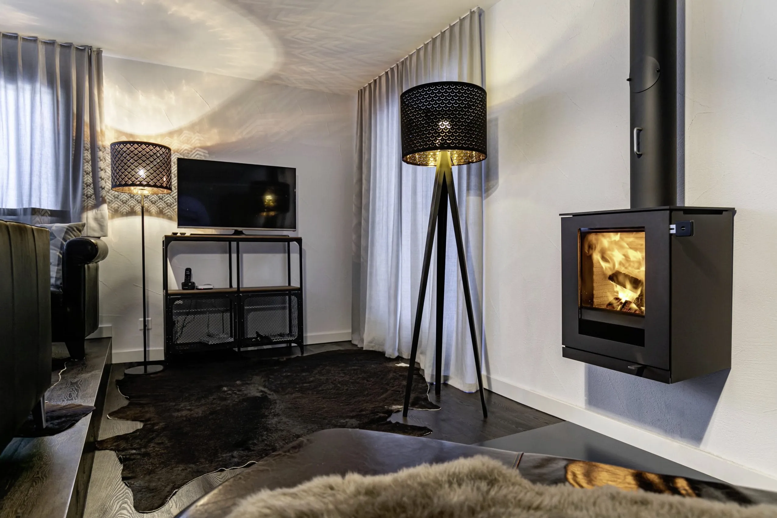 Wohnzimmer des Chalet vue au lac mit kleinem Kamin, zwei schwarzen Stehlampen, Fell auf dem Boden und TV